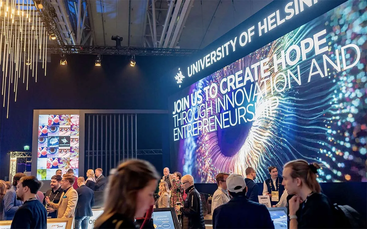 Yleisöä ja suuri näyttö tekstillä 'University of Helsinki – Join us to create hope through innovation and entrepreneurship' Slush/AI Summit -tapahtumassa, jossa HelsinkiTechin tiimi on mukana